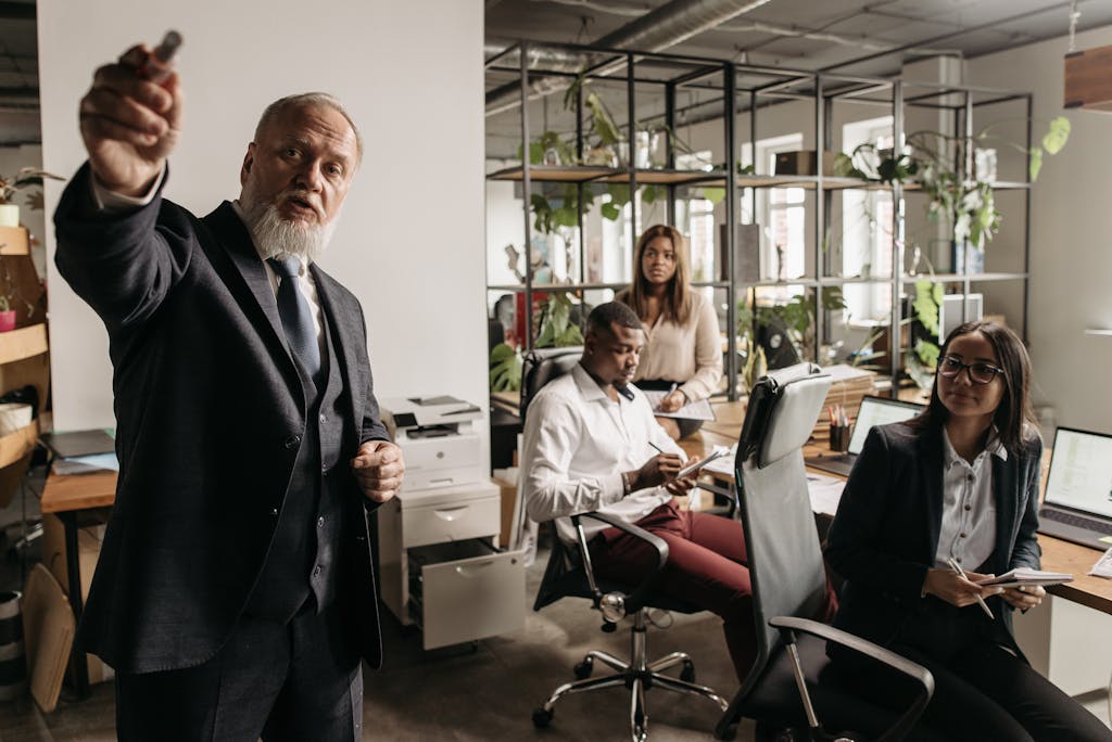 A diverse team in a modern office setting engaged in a business meeting with a senior leader presenting.